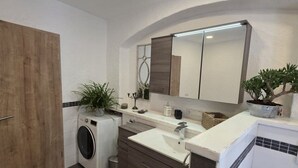 A modern bathroom with a built-in washing machine, a large mirror, and a shower area. - Vrbo Property (Weißenstadt)