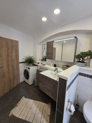 Une salle de bain moderne équipée d’un lave-linge intégré, d’un grand miroir et d’un espace douche.