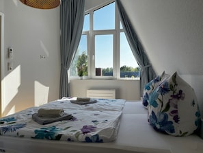 Une chambre à coucher avec un lit, un radiateur, une fenêtre avec des rideaux et une vue sur l’extérieur.