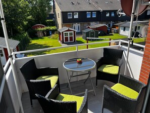 Un balcon avec des fauteuils en osier et une table, donnant sur une pelouse verdoyante et des maisons.