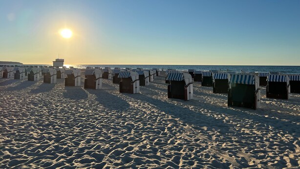 Ein Strand mit Reihen von Strandkörben und einem klaren Himmel.