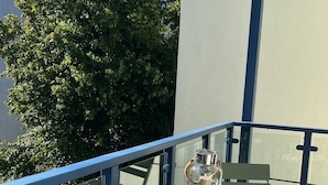 Ein Balkon mit Tisch und Stühlen, einer Glasflasche und einem Baum.