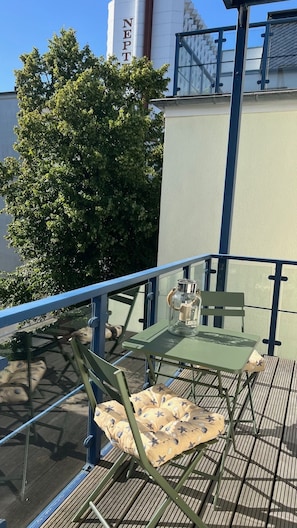 A balcony with a table and chairs, a glass bottle, and a tree. - Vrbo Property (Rostock)