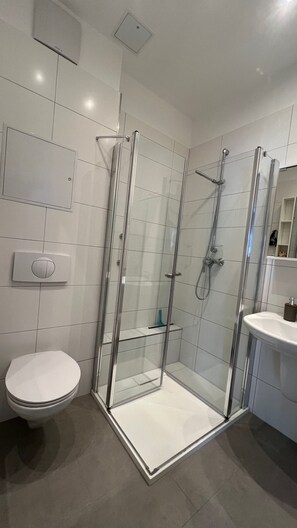 A modern bathroom with a glass-enclosed shower, a toilet, and a sink. - Vrbo Property (Rostock)
