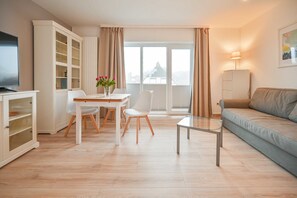 Un salon moderne comprenant un coin repas, un canapé, un téléviseur et un meuble avec des portes en verre.