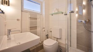 A modern bathroom with a white sink, toilet, and glass shower enclosure. - Vrbo Property (Kellenhusen)