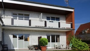 A two-story residential building with a balcony, sliding glass doors, and a small garden area with outdoor furniture. - Vrbo Property (Kellenhusen)