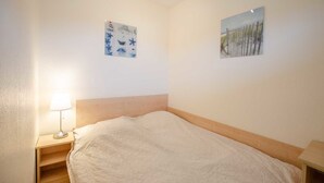 A bedroom with a bed, a nightstand, a lamp, and two wall art pieces. - Vrbo Property (Kellenhusen)