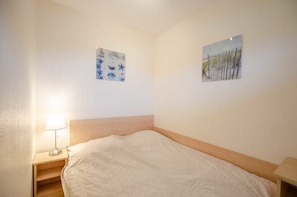 Une chambre à coucher comprenant un lit, une table de chevet, une lampe et deux œuvres d’art murales.