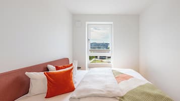 Et hotelværelse med seng, puder, udsigt ud og en dør.