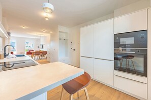 Eine moderne Küche mit weißen Schränken, einem eingebauten Ofen und einem Essbereich mit Tisch und Stühlen.