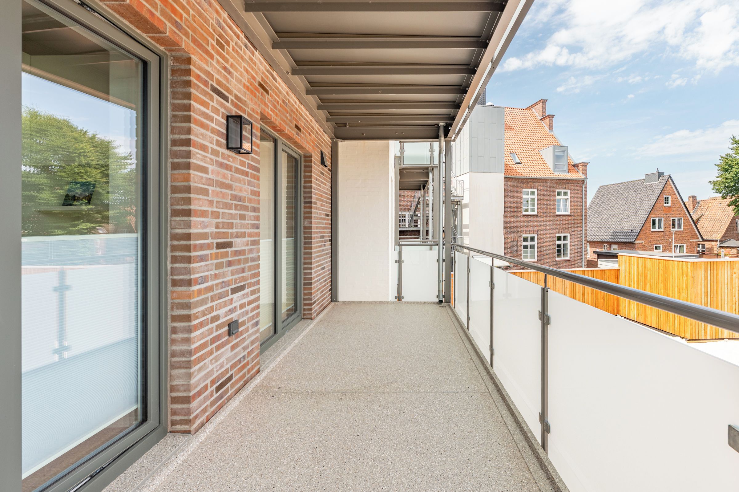 Ein Balkon mit Blick auf ein Backsteingebäude und einen Holenzaun.