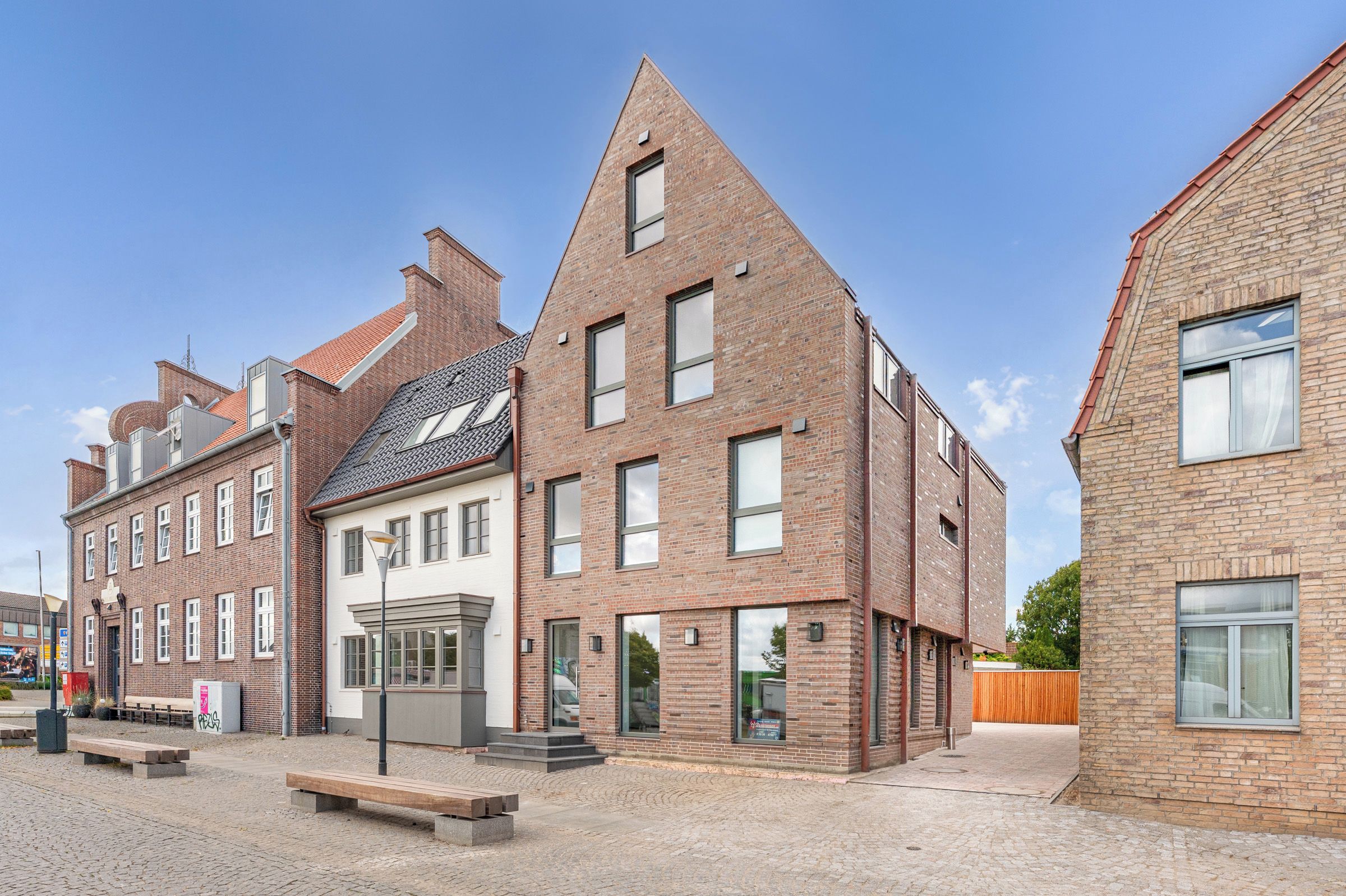 Eine Straße mit traditionellen Backsteingebäuden, einer Bank und blauem Himmel.