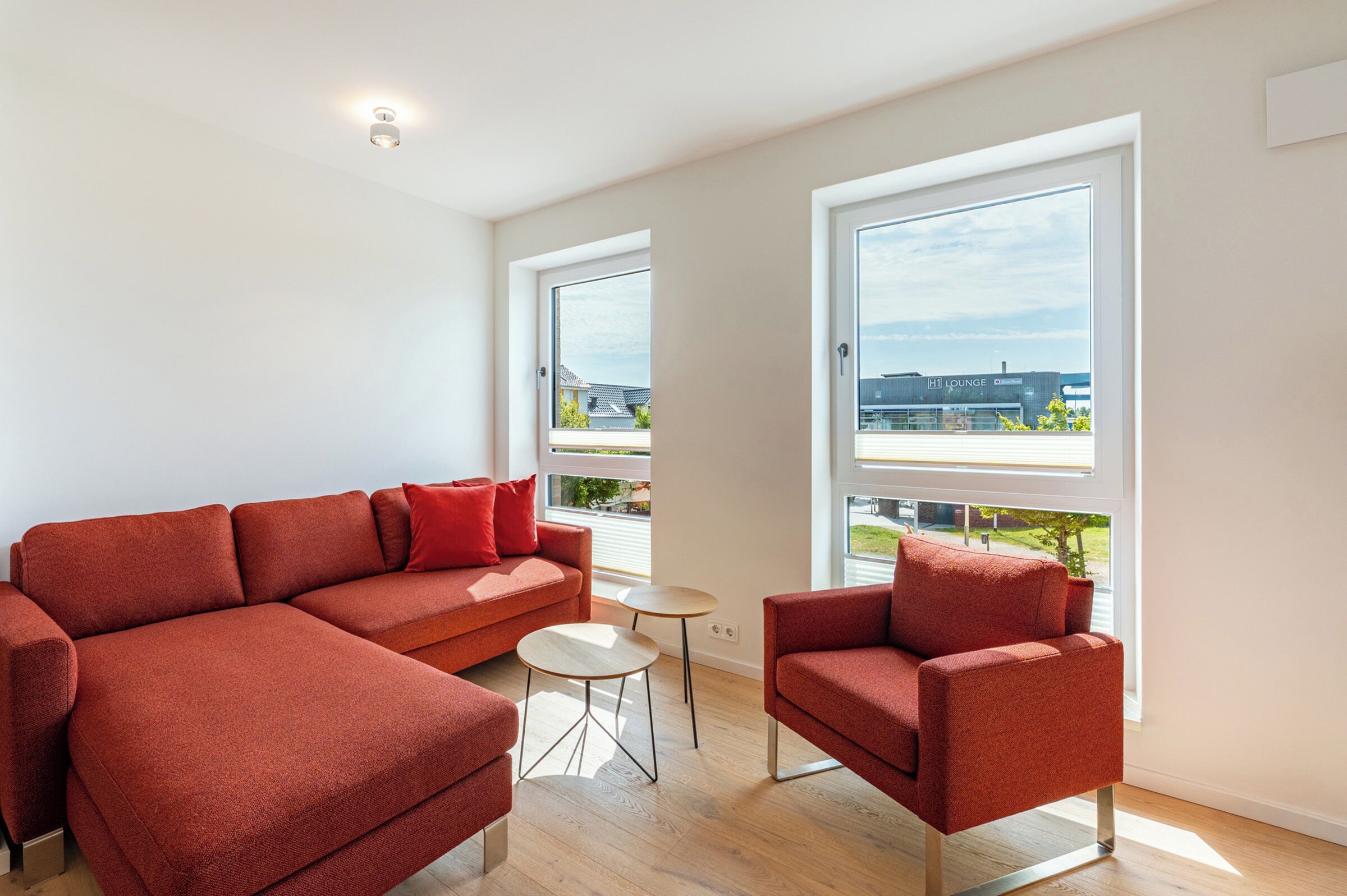 Un salon moderne avec un canapé rouge, une petite table ronde et de grandes fenêtres donnant sur la ville.