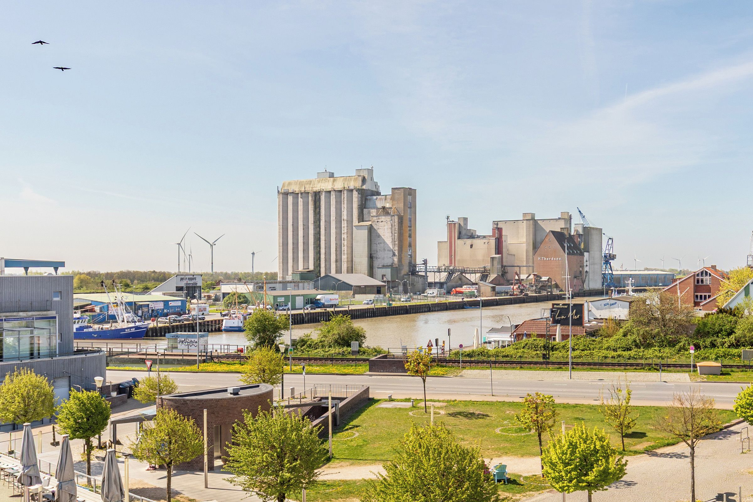 A riverside view of a city with industrial buildings, a bridge, and boats.