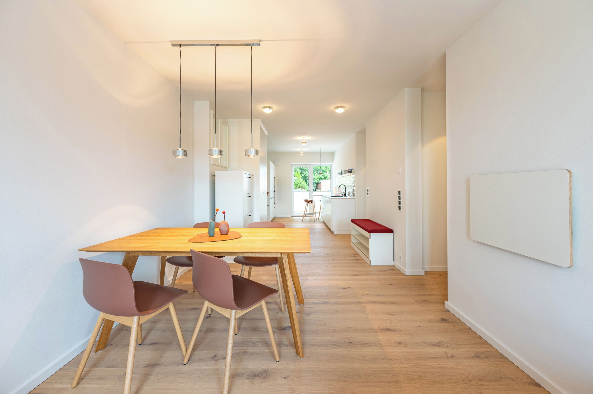 Eine moderne Küche mit weißen Schränken, einem Holzespeisetisch mit Stühlen und Pendelleuchten.