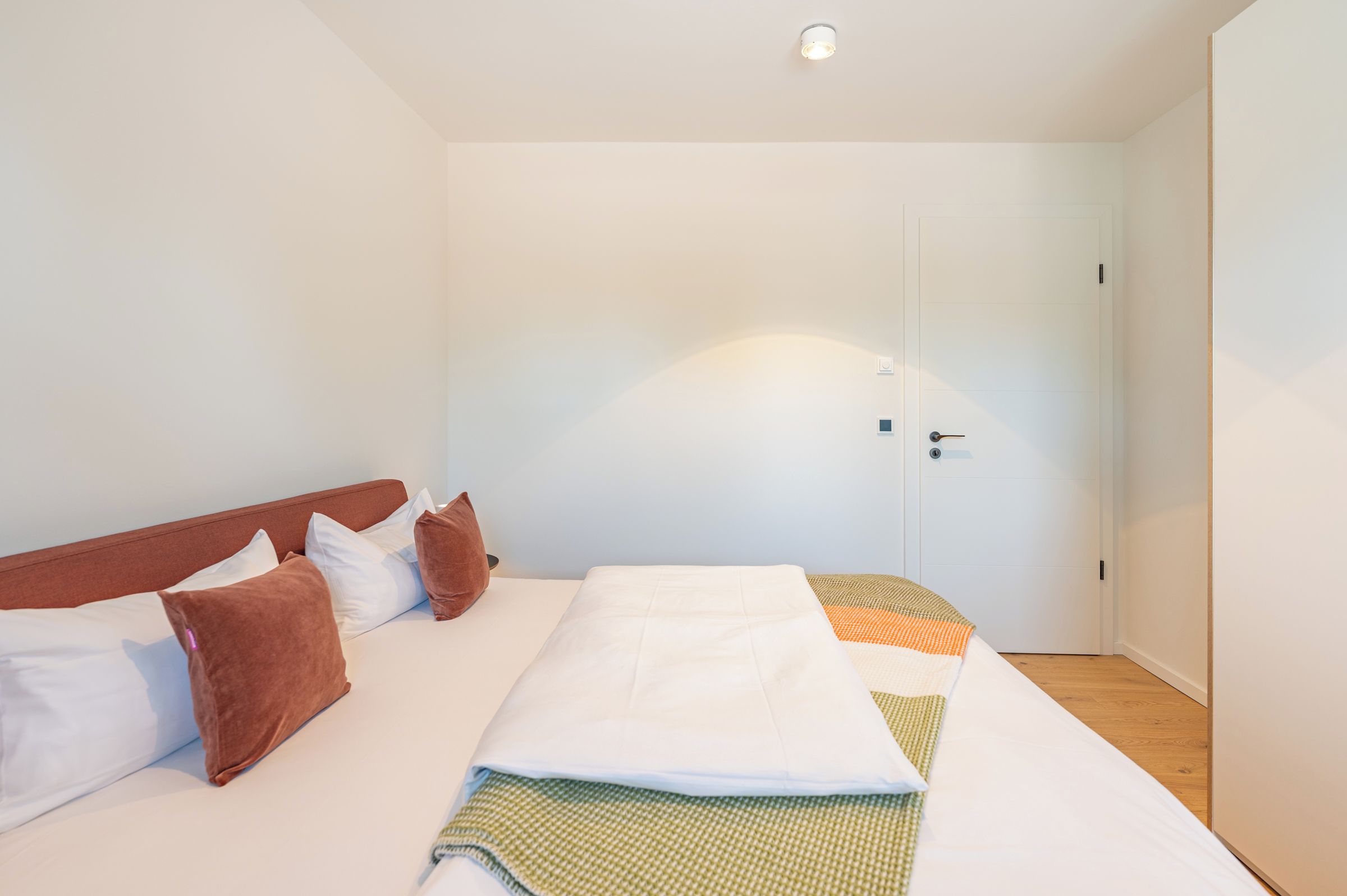 A bedroom with a bed, pillows, a door, and a light fixture.
