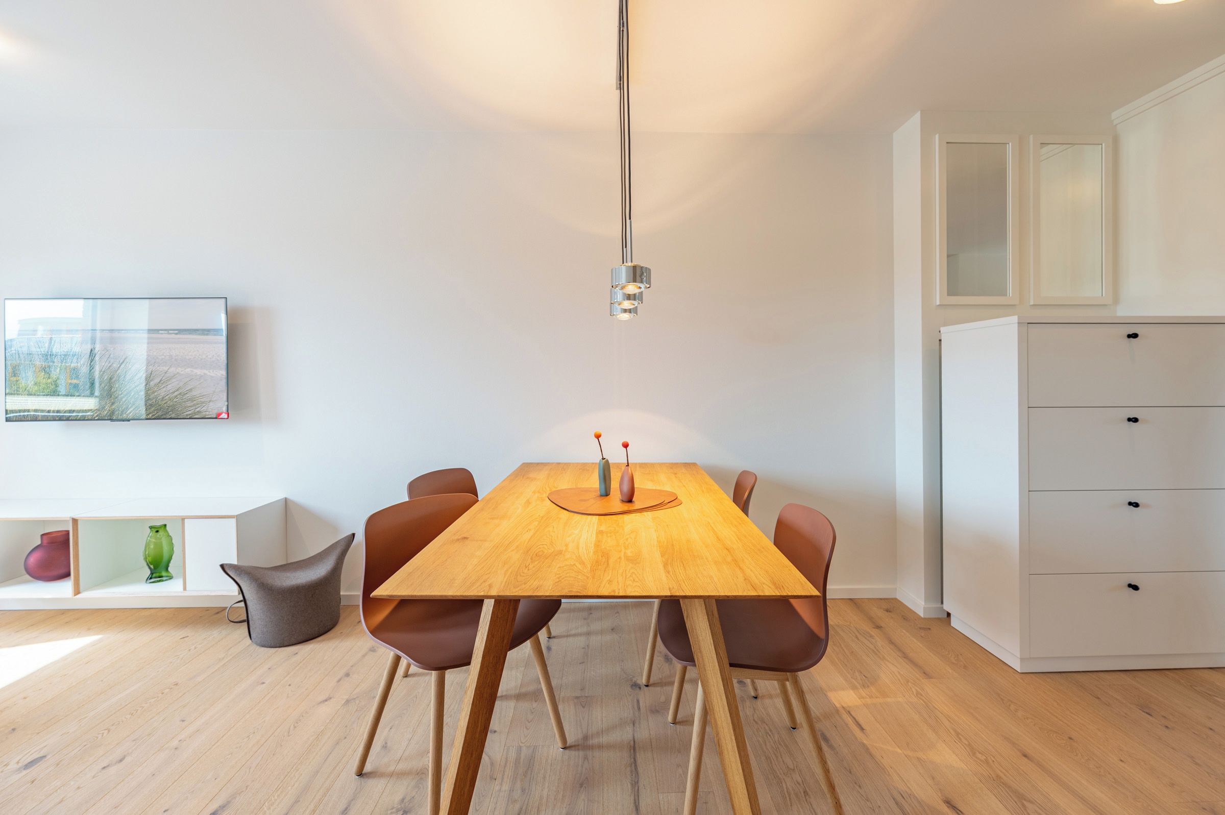 Ein moderner Essbereich mit einem Holztisch, vier Stühlen, einer Vase und einem Gemälde an der Wand.