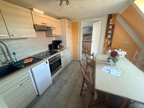 A compact kitchen with modern appliances, a dining area with a table and chairs, and a view of a balcony. - Vrbo Property (Kägsdorf)