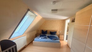 Ein Schlafzimmer mit schrägem Dach, einem Bett, einem Nachttisch, einer Lampe und einem Babybett.