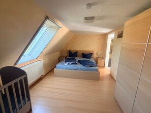 A bedroom with a sloped ceiling, a bed, a nightstand, a lamp, and a crib. - Vrbo Property (Kägsdorf)