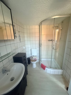 A bathroom with a white sink, a toilet, and a glass-enclosed shower. - Vrbo Property (Kägsdorf)