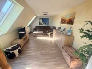 A modern living space with a sloped ceiling, a television, a sofa, a coffee table, and a kitchen area with a countertop and cabinets. - Vrbo Property (Kägsdorf)