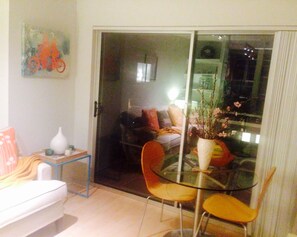 Ein Wohnzimmer mit Glastür, die auf einen Balkon führt, einem weißen Sofa, einem kleinen Tisch mit einer Vase und einem Sessel.