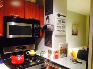 Een keuken met een magnetron, fornuis en waterkoker. Er staan boeken en een poster aan de muur.