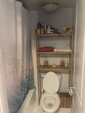 Ein kleines Badezimmer mit Toilette, Ablage für Toilettenartikel und einer Duschvorhang.