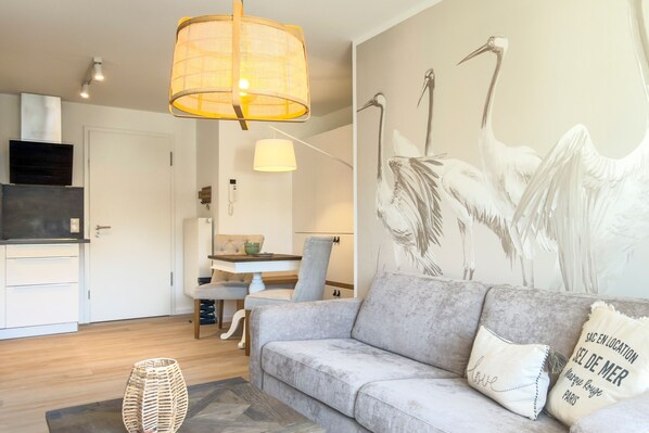 A modern living room with a grey sofa, a woven floor lamp, and a wall mural of birds. - Vrbo Property (Zingst)