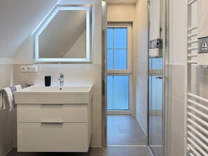 A modern bathroom with a large mirror, a sink, and a shower area. - Vrbo Property (Zingst)