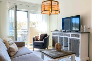 A living room with a sofa, armchair, coffee table, TV, and a cabinet with decorative items. - Vrbo Property (Zingst)
