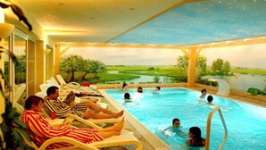 Un área de piscina con sillones de descanso y gente nadando.