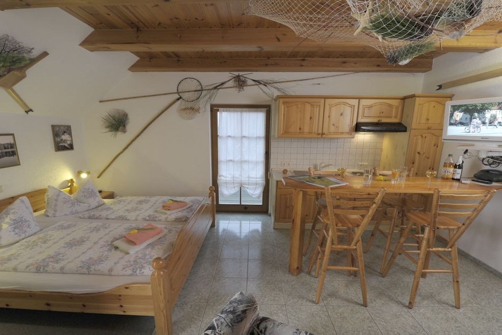 A room with a bed, wooden furniture, a kitchen area, and a television.