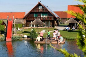 Ein hölzernes Gebäude mit einem strohgedeckten Dach, einem Schwimmbad und einem Steg mit Stühlen.