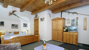 Una habitación con una cama de madera, una mesita con una botella y un vaso, armarios de madera y un televisor.