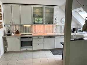 A kitchen with white cabinets, a built-in oven, and a coffee machine. - Vrbo Property (Cloppenburg)