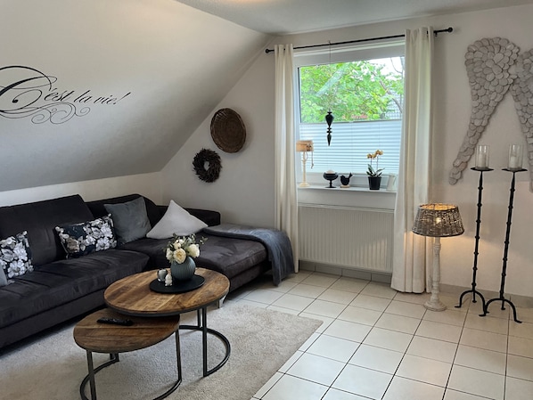 A modern living room with a dark sofa, a round wooden coffee table, and a window with a view of greenery. - Vrbo Property (Cloppenburg)