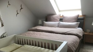 A bedroom with a crib, a bed with pillows, a bedside table, and a lamp. - Vrbo Property (Cloppenburg)