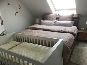 A bedroom with a crib, a bed with pillows, a bedside table, and a lamp. - Vrbo Property (Cloppenburg)