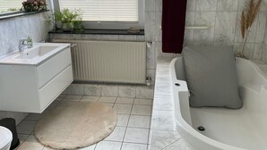 A modern bathroom with a bathtub, a sink, a window, and a radiator. - Vrbo Property (Cloppenburg)