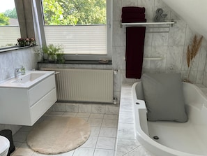 A modern bathroom with a bathtub, a sink, a window, and a radiator. - Vrbo Property (Cloppenburg)