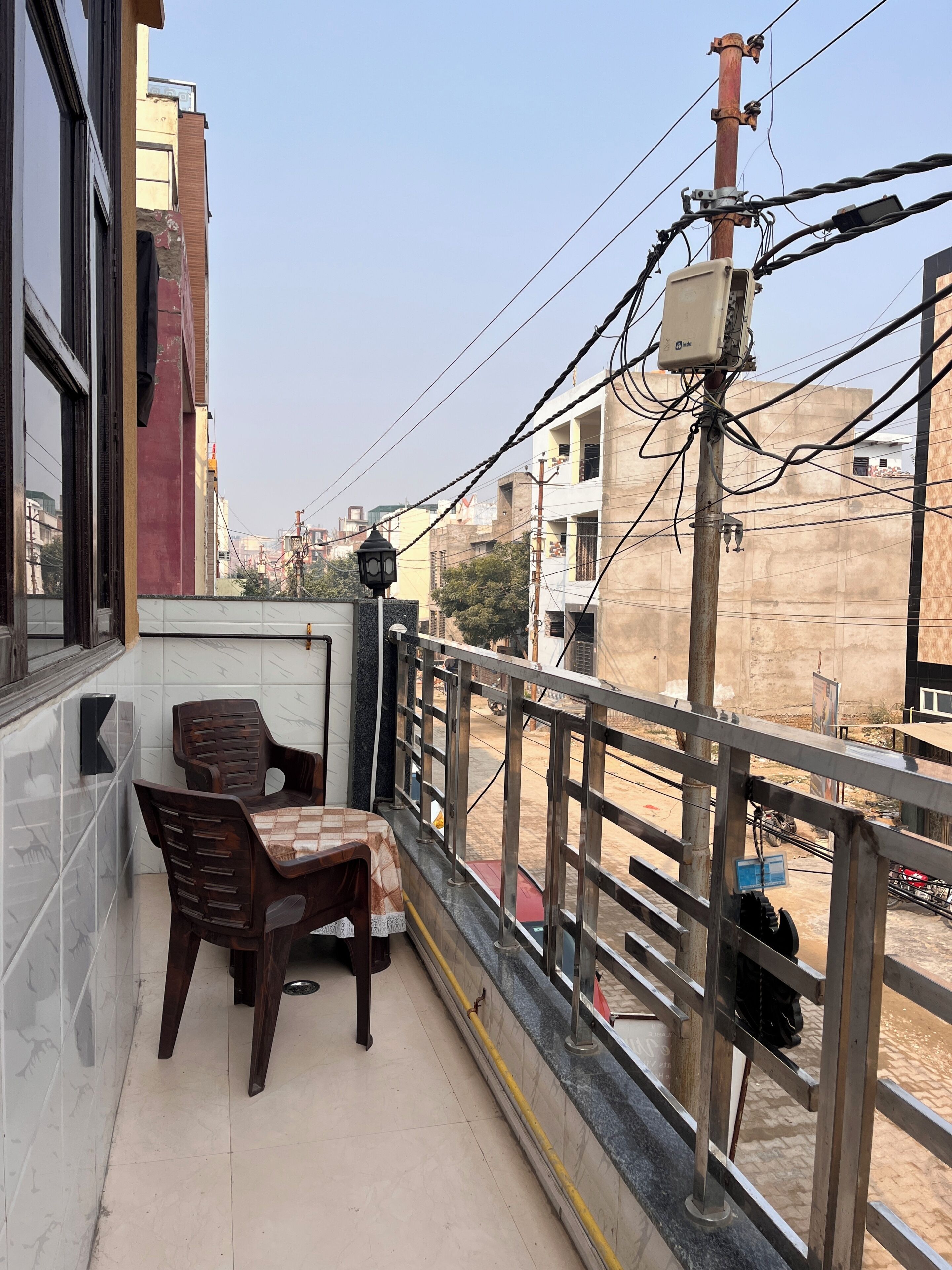 A balcony with a table and chairs, a view of the street, and a building in the background.