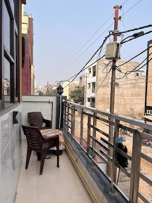 Un balcón con mesa y sillas, vista a la calle y un edificio al fondo.