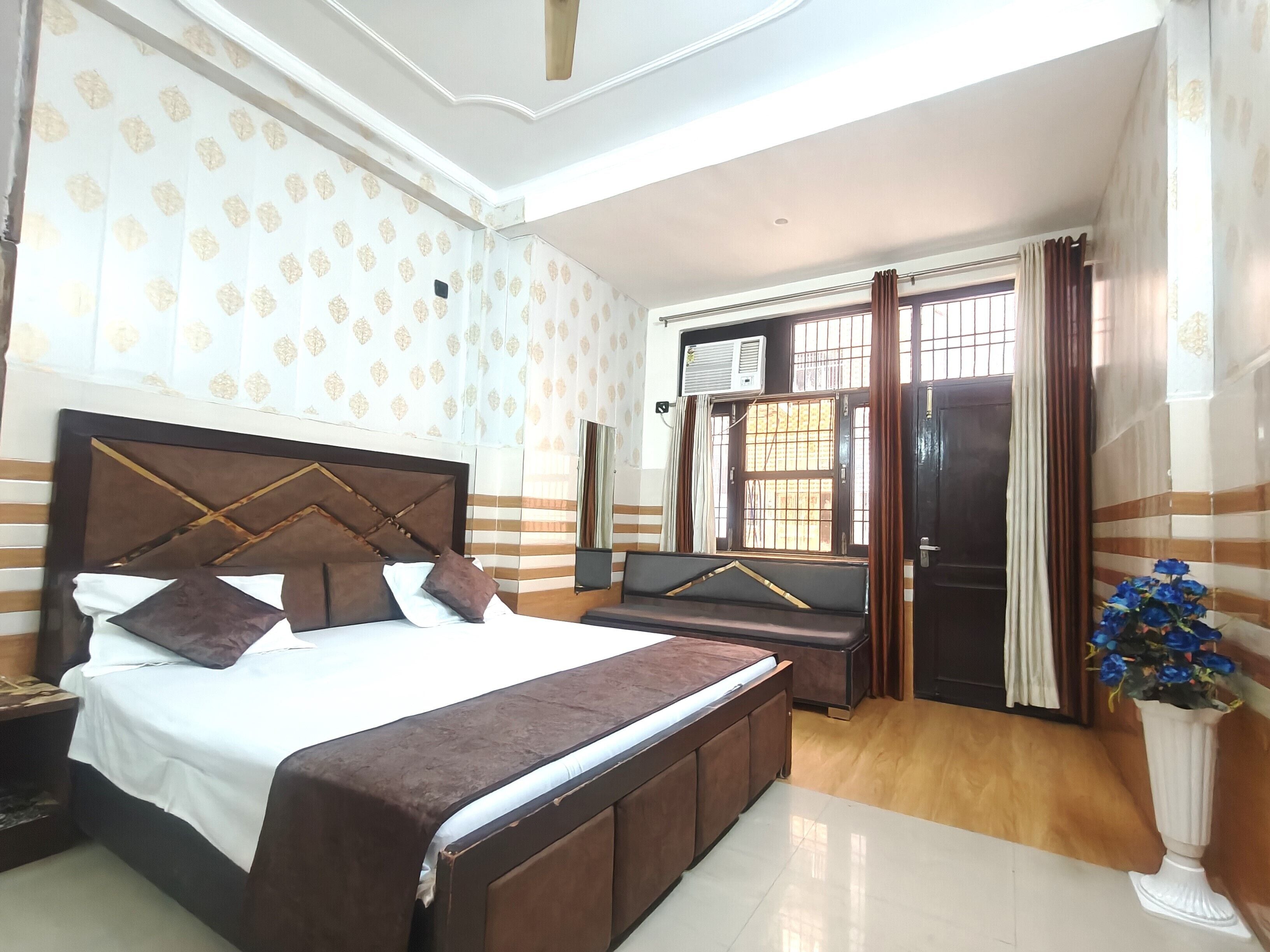 A hotel room with a bed, a seating area, a window with curtains, and a potted plant.