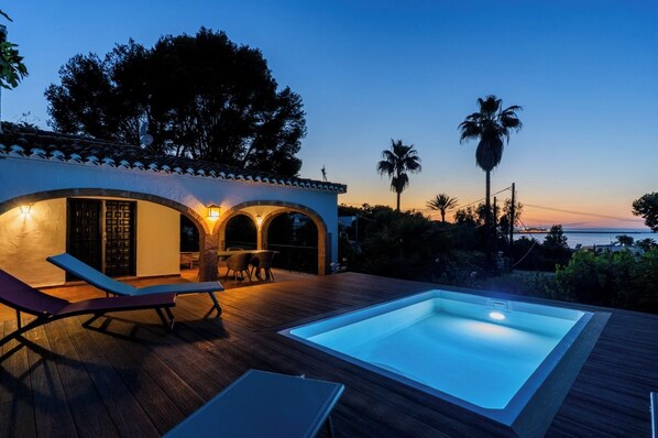 A poolside area with a wooden deck, a lounge chair, and a table.
