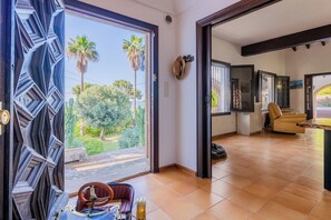 A spacious room with a large sliding glass door leading to a garden, a comfortable seating area with a sofa and armchairs, and a kitchen area visible through the door.