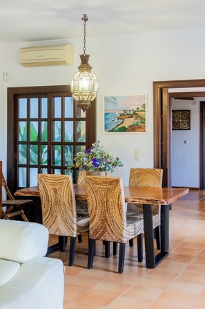 A dining area with a wooden table, woven chairs, a hanging light fixture, and a painting on the wall. - Vrbo Property (VC)