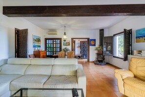 A spacious living room with a sofa, a coffee table, and a fireplace. There is a dining area with chairs and a table. - Vrbo Property (VC)